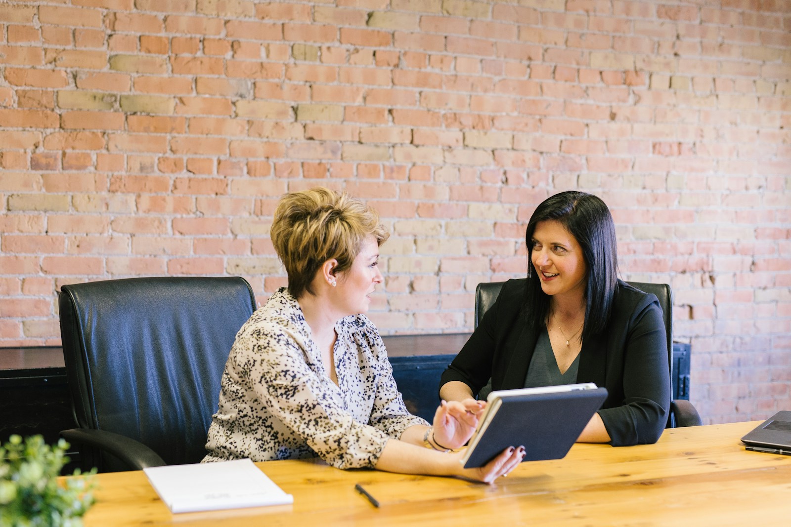 two women in an recruitment agency sitting on leather chairs in front of table as they search for a new career