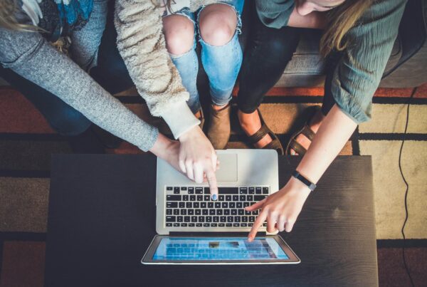 Three people pointing at a silver computer screen
