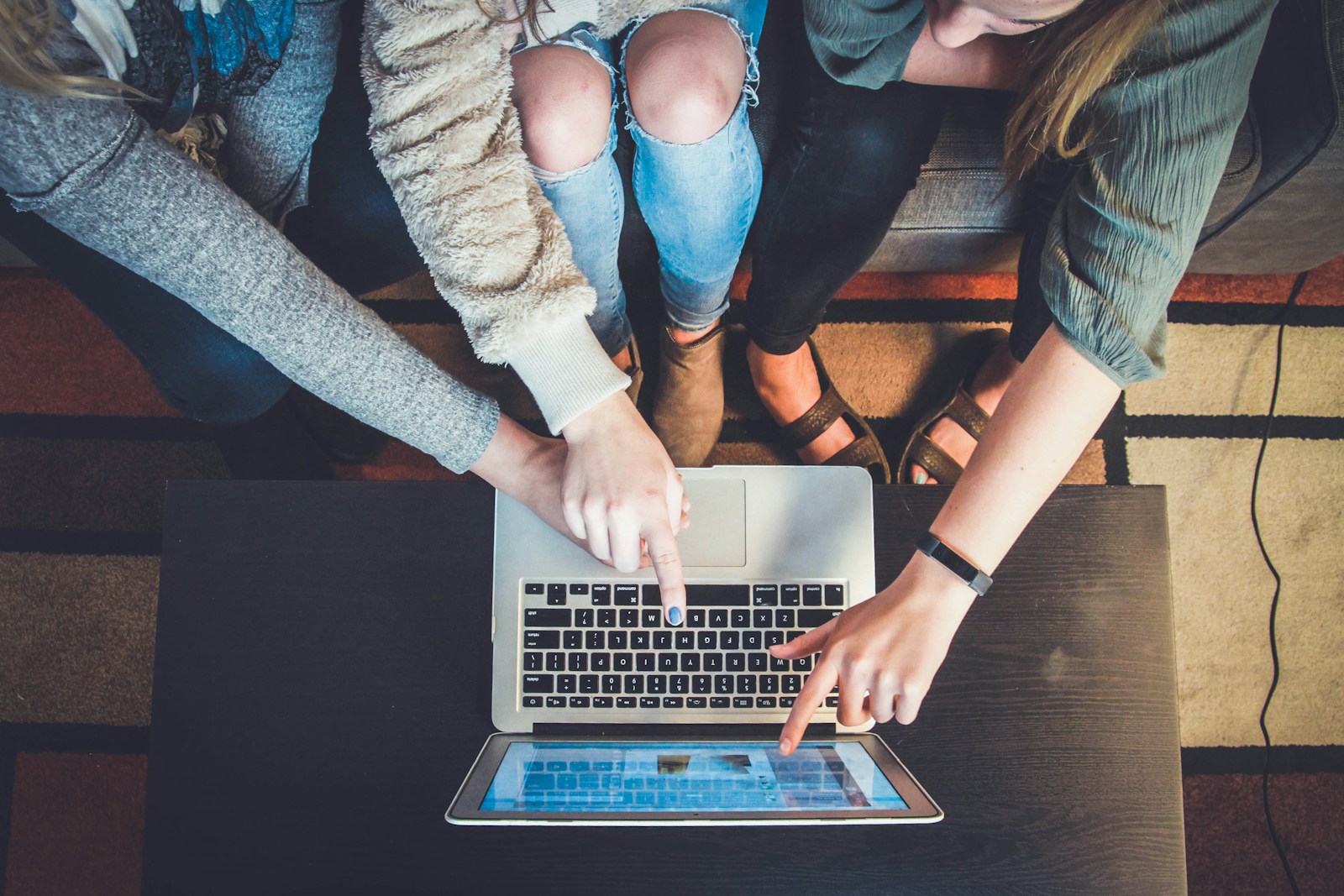 Three people pointing at a silver computer screen